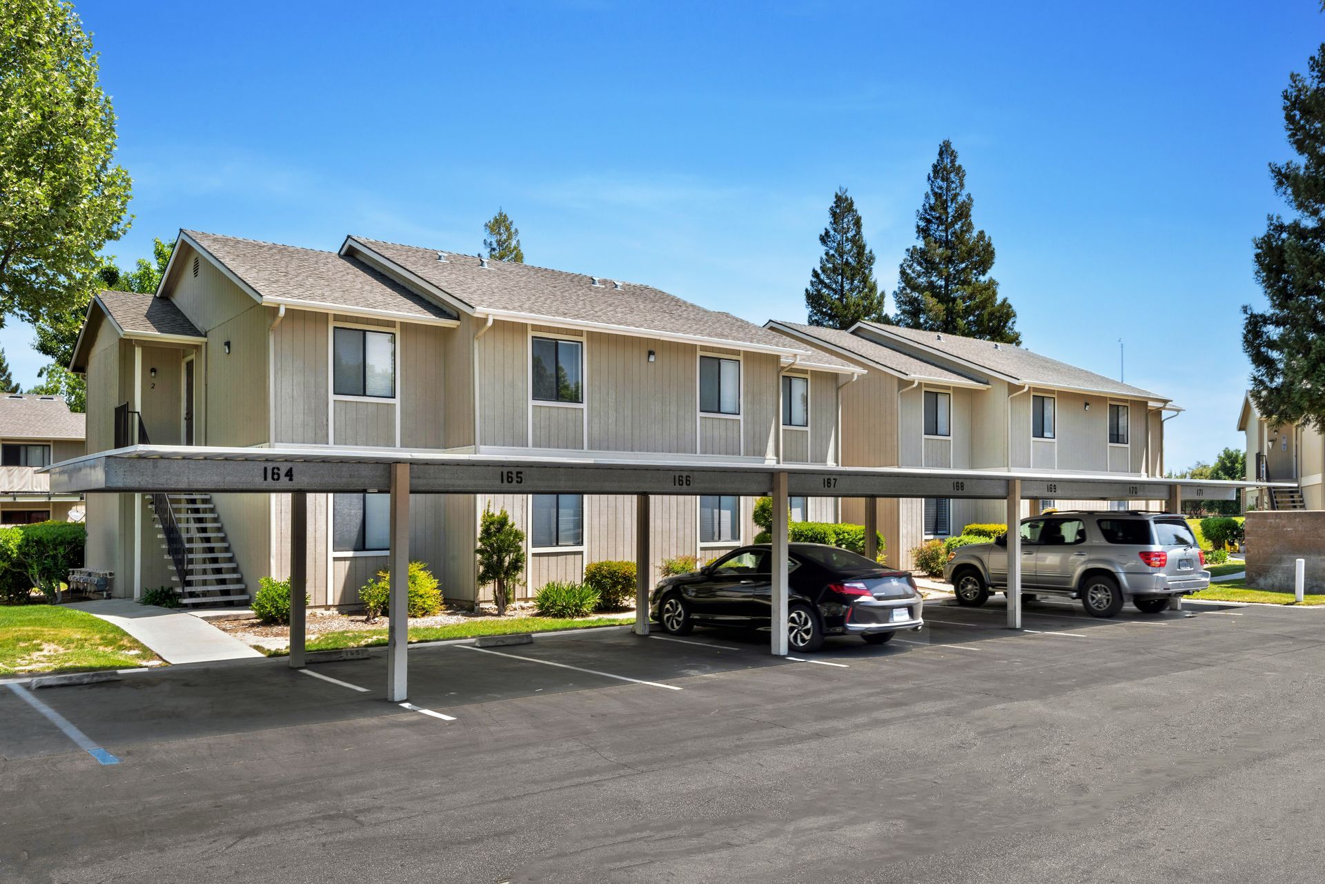 Parking lot with covered parking spaces, beige apartment building, blue sky.