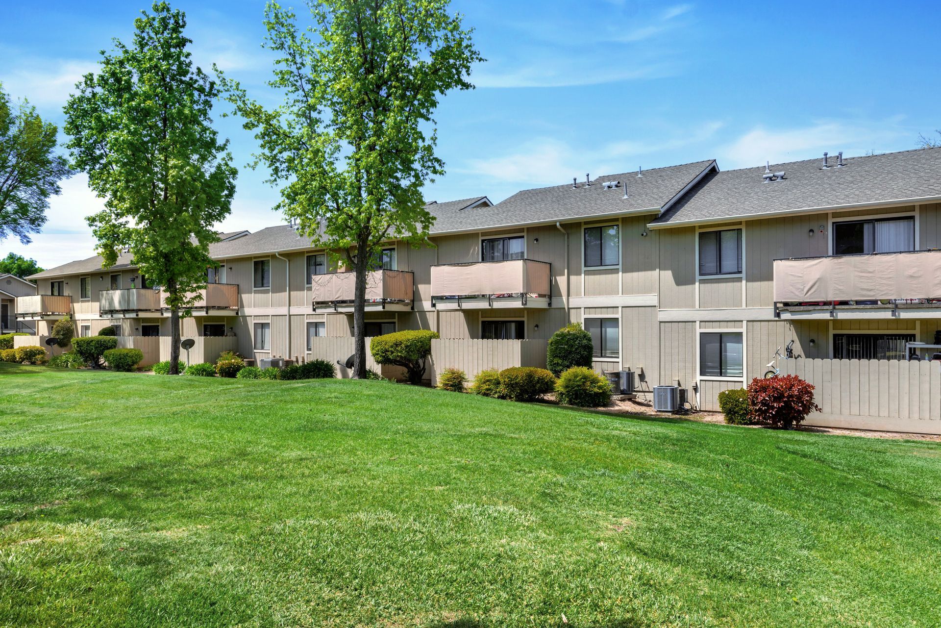 Row of beige townhouses with green lawn, blue sky, and trees.