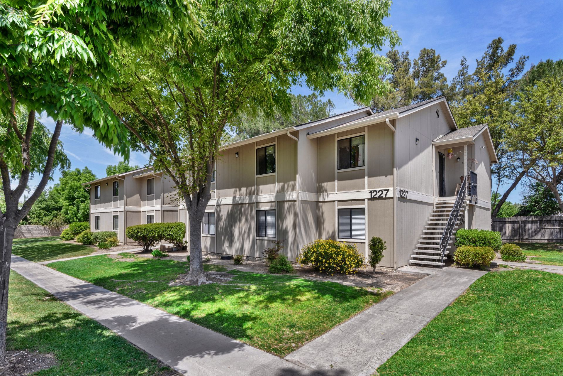 Apartment building exterior with beige walls, stairs, green lawn and trees. Blue sky.