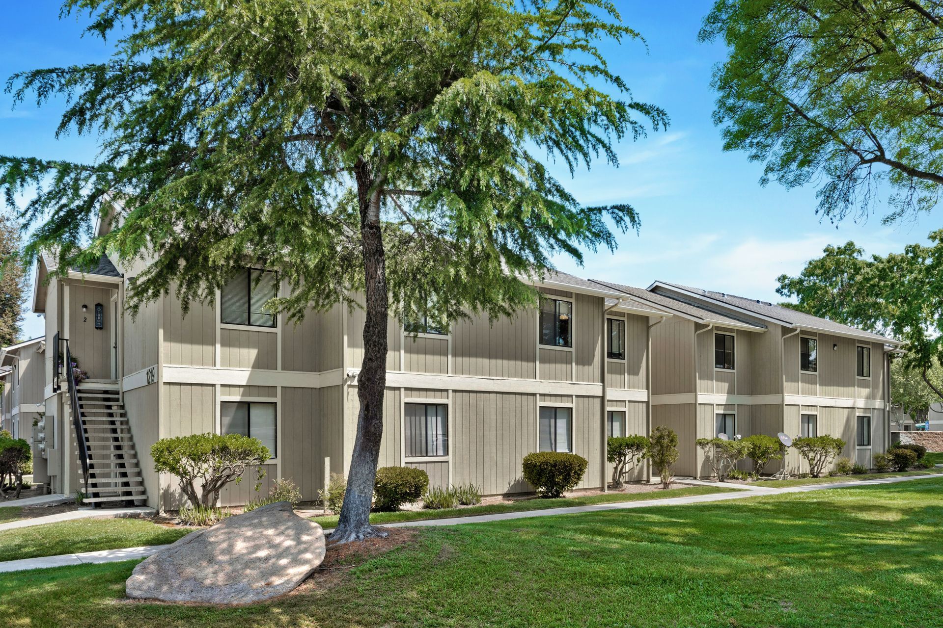 Two-story apartment building with beige siding and green lawn.