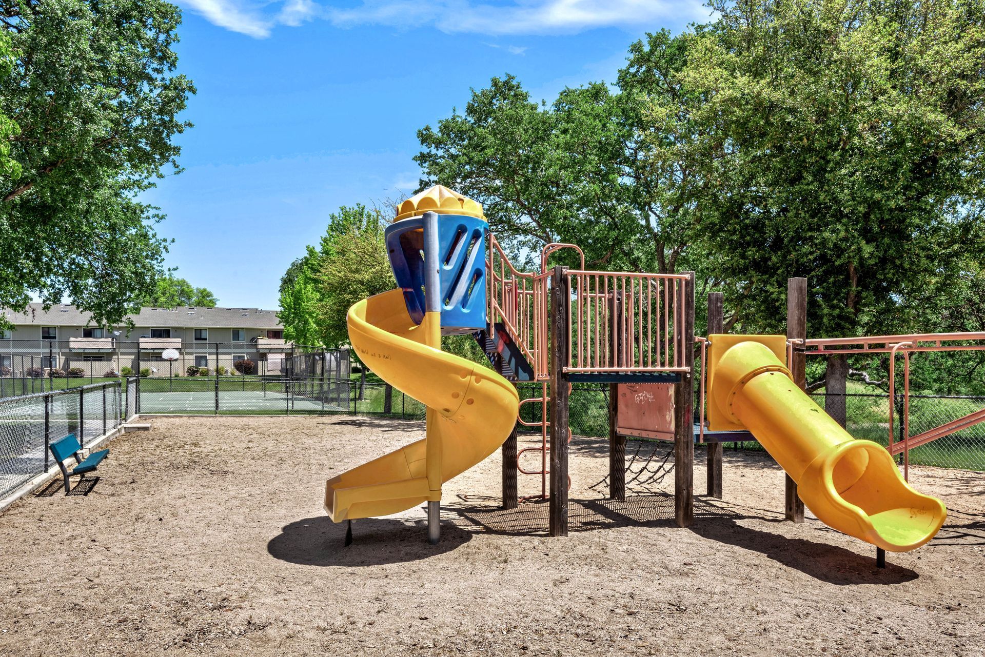 Playground with yellow slides, climbing structure, and soft ground in a park setting.