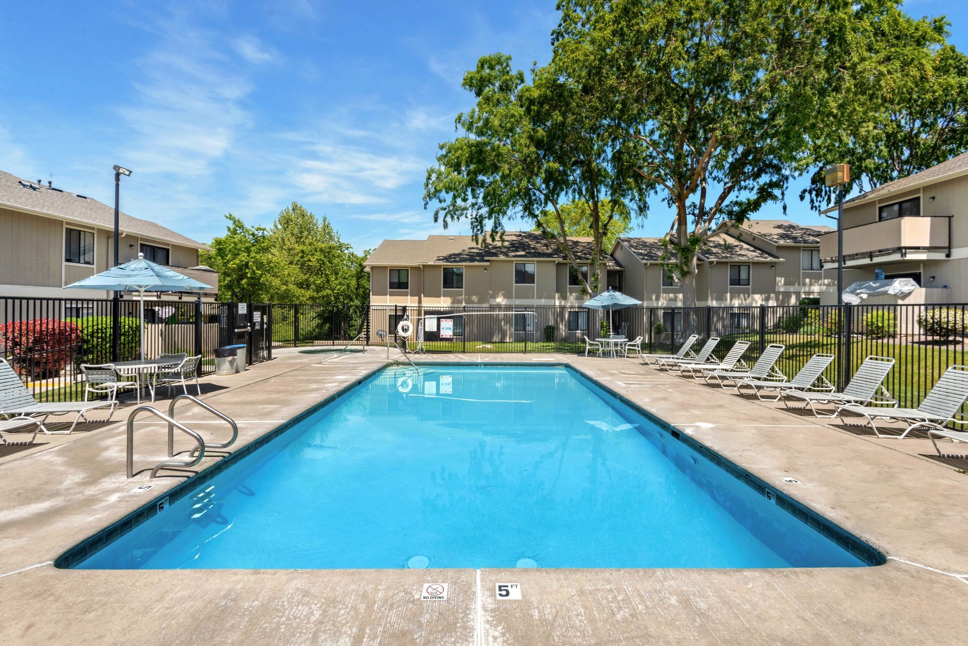 Swimming pool surrounded by lounge chairs and apartment buildings on a sunny day.