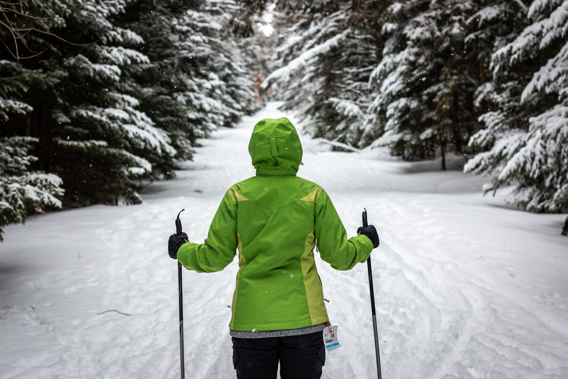 A person in a green jacket is cross country skiing in the snow.
