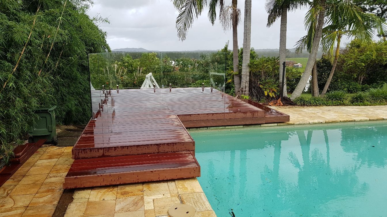 A Swimming Pool with A Wooden Deck and Palm Trees in The Background — Tuggerah Lakes Glass In Tumbi Umbi, NSW