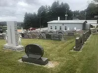 Cemetery with headstones and a small white building in the background. Overcast sky.