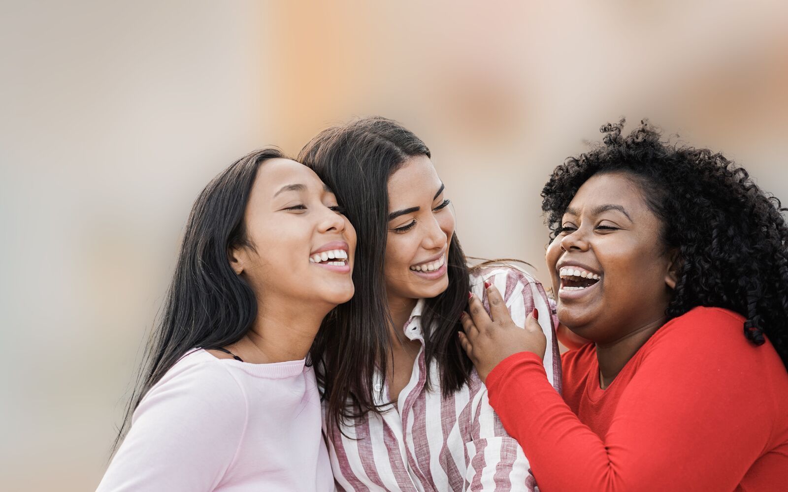 Three women are laughing together and hugging each other.