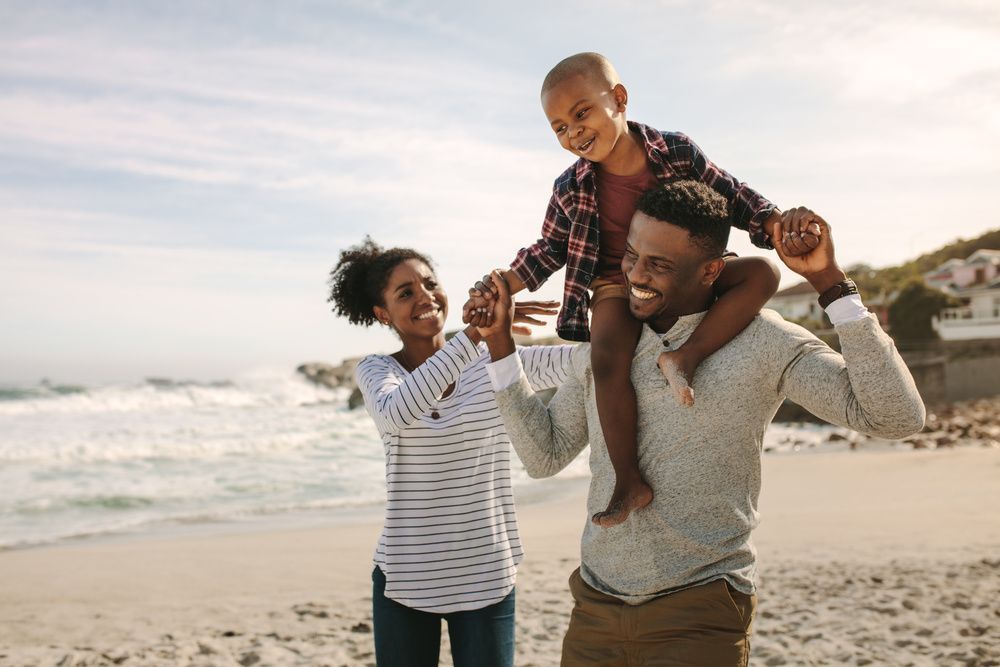 Family playing on a beach at sunset, with a child sitting on an adult’s shoulders.
