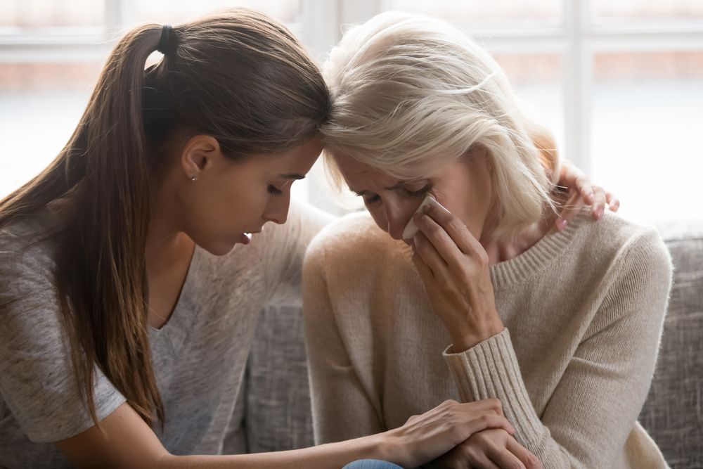 Two women sitting close together, one comforting the other who is crying