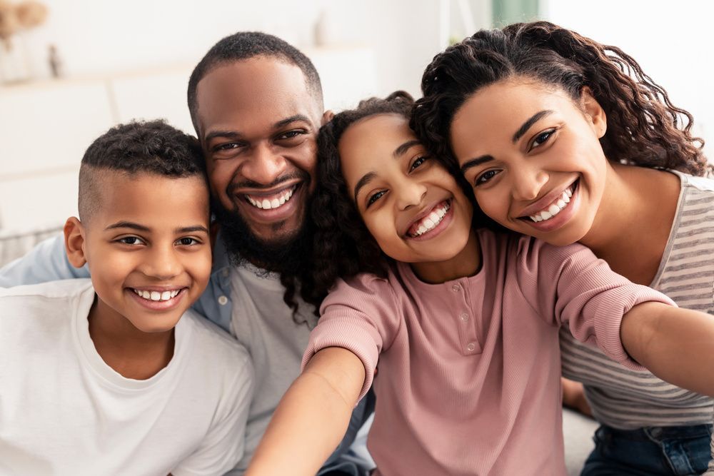 Four smiling people leaning together on a couch, posing for a close family selfie