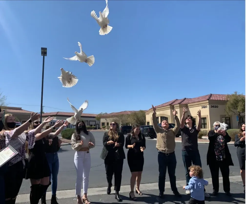 Group releases white doves into a sunny sky outside a building
