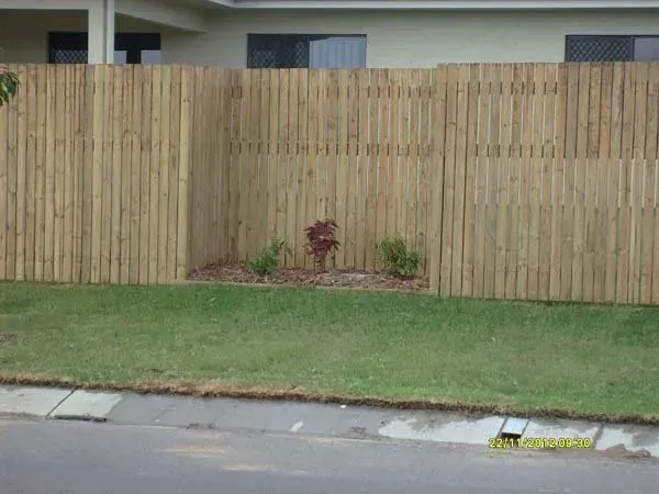A Wooden Fence Surrounds a Lush Green Lawn in Front of A House — Fencing Around Town Townsville in Garbutt, QLD