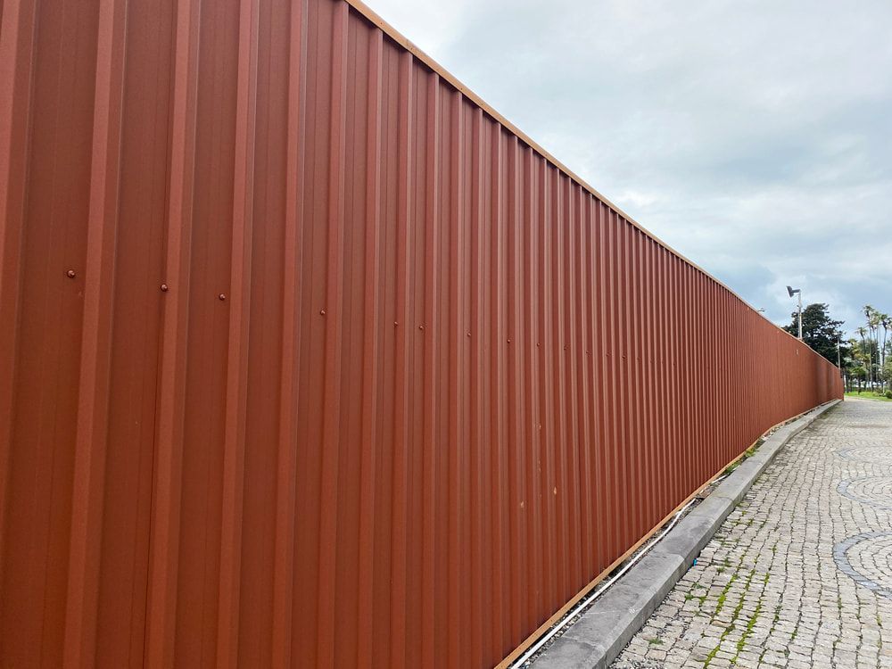 A Long Red Metal Fence Along a Cobblestone Street — Fencing Around Town Townsville in Garbutt, QLD