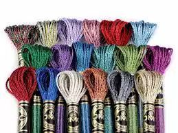 Una colorata collezione di matassine di filo da ricamo DMC disposte su due file su sfondo bianco.