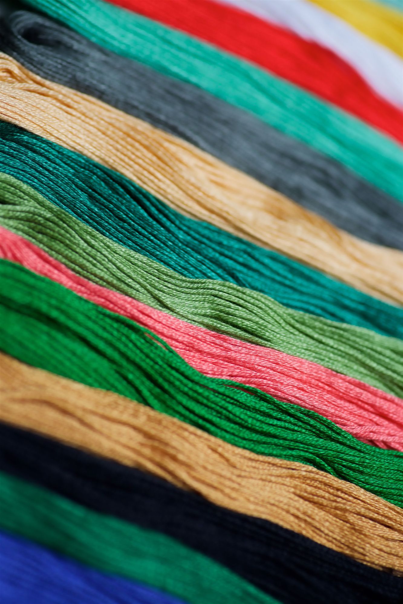 Una collezione di matassine di filo da ricamo colorato disposte in diagonale, con una sfumatura di rosso, verde, oro e blu.