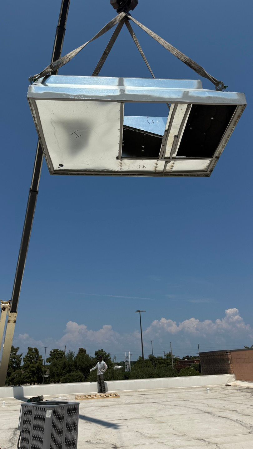 White air conditioning unit, with fan, sits on black blocks near a window. White air conditioning unit, with fan, sits on black blocks near a window.