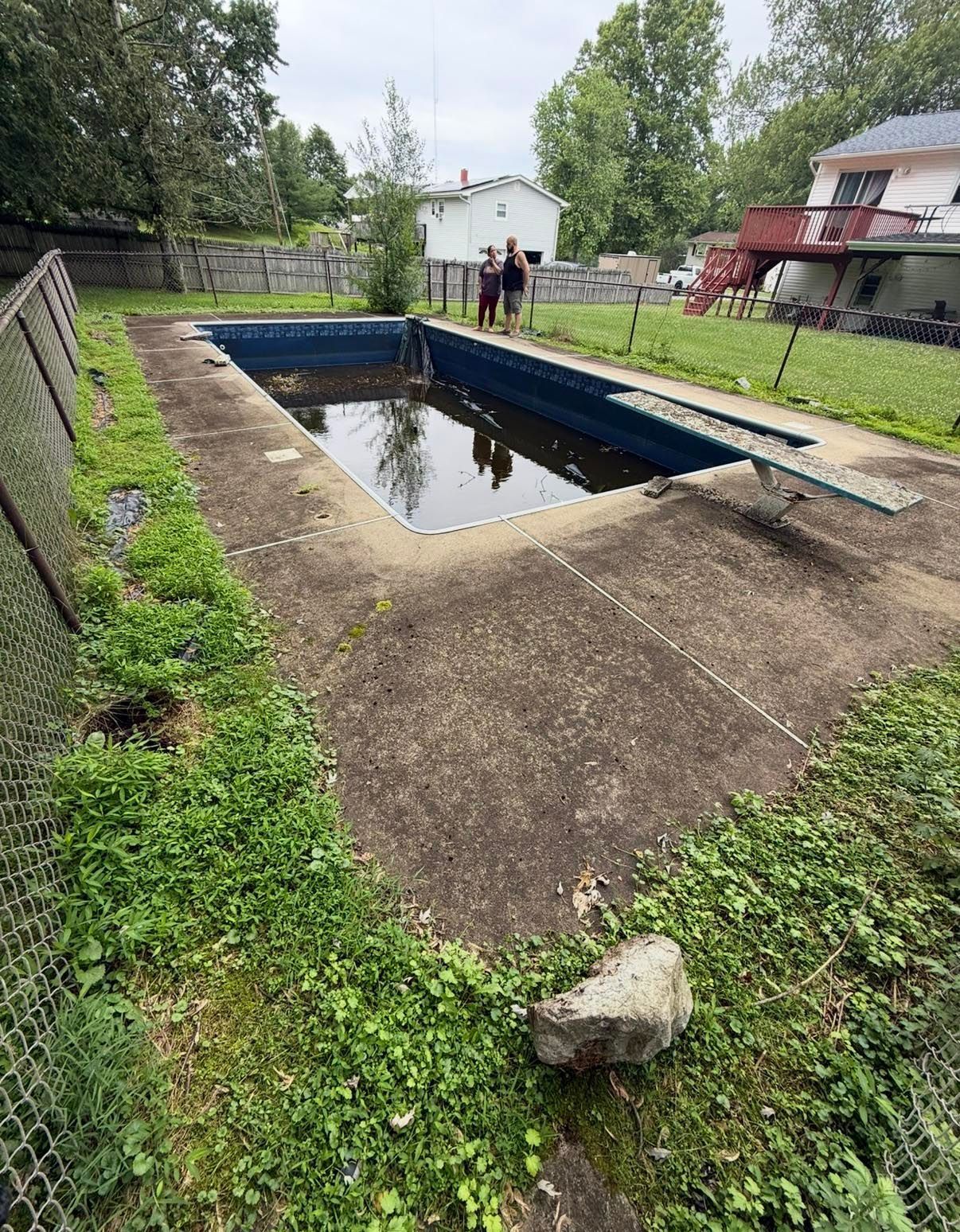 Pool surrounded by speckled concrete and greenery, nestled in a wooded area.