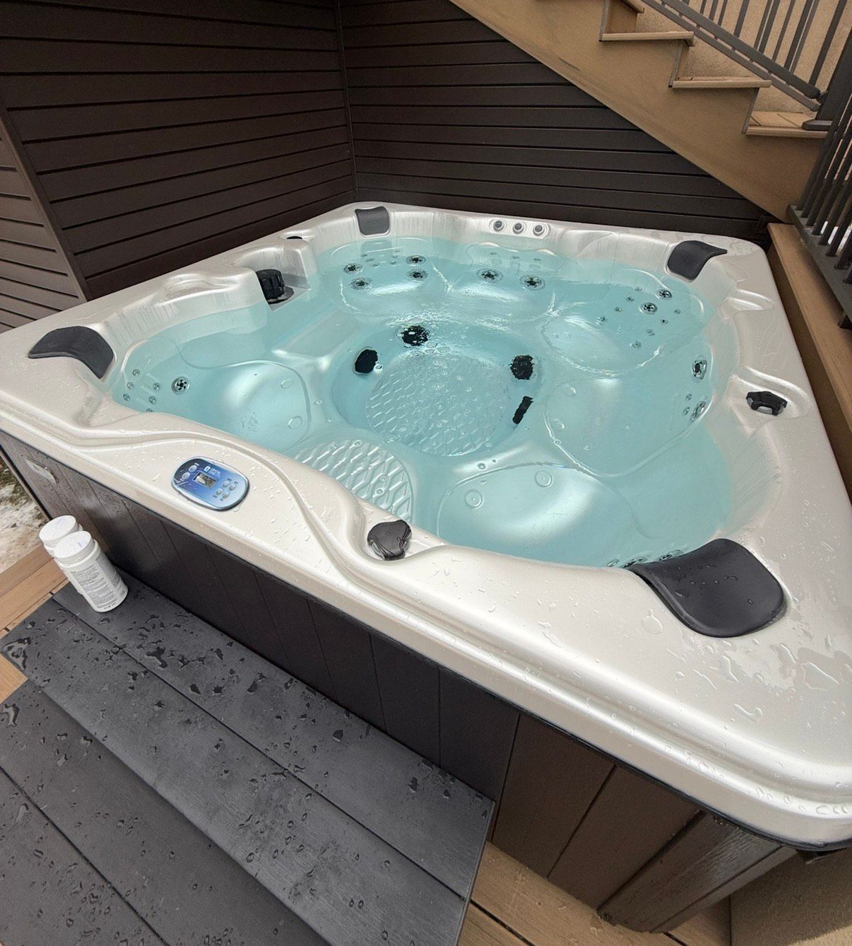 Hot tub filled with water on a wooden deck, next to stairs and a railing.