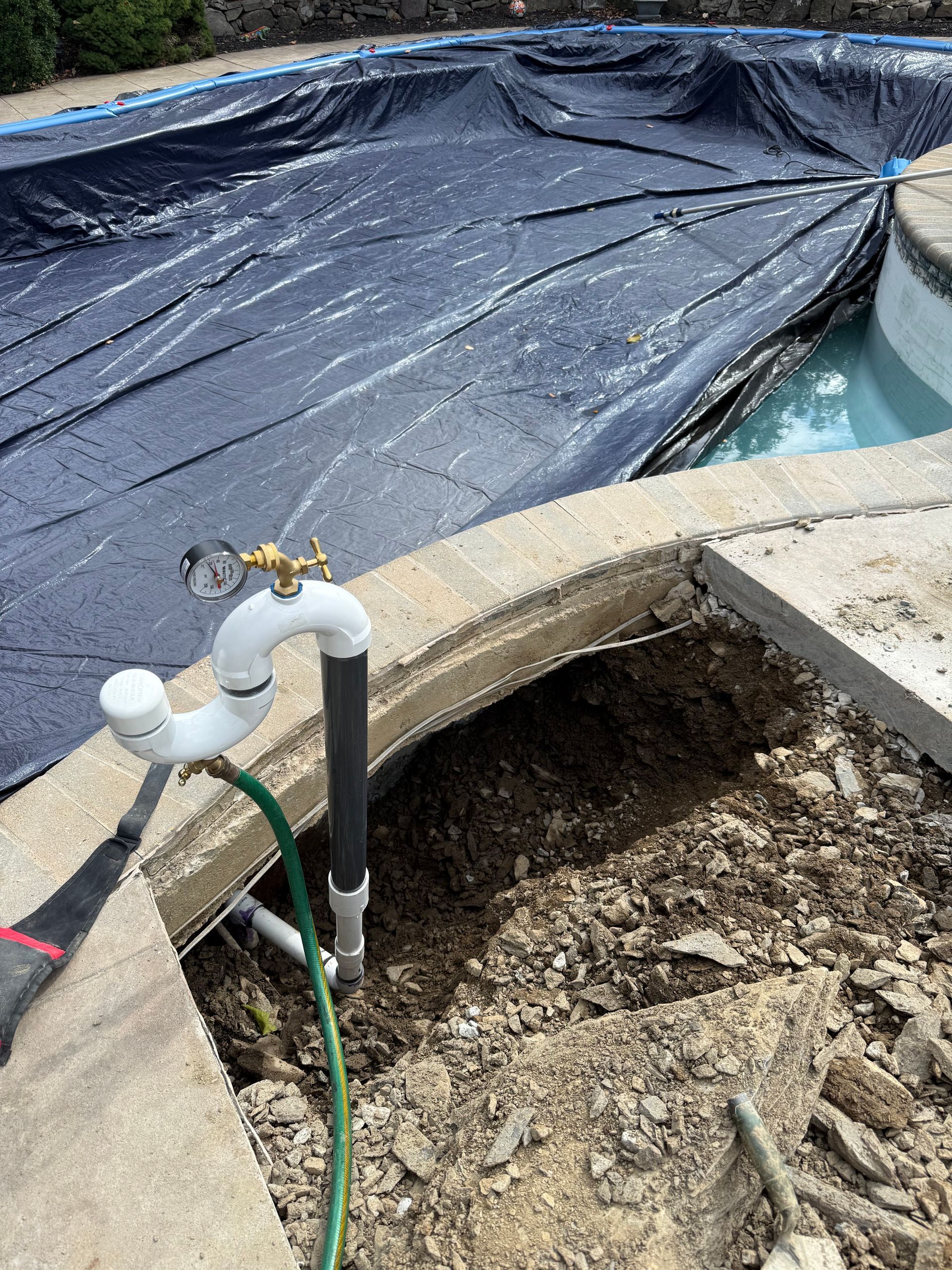 Pool equipment in a fenced enclosure: filter, pump, pipes. Blue and tan. Wooden fence.