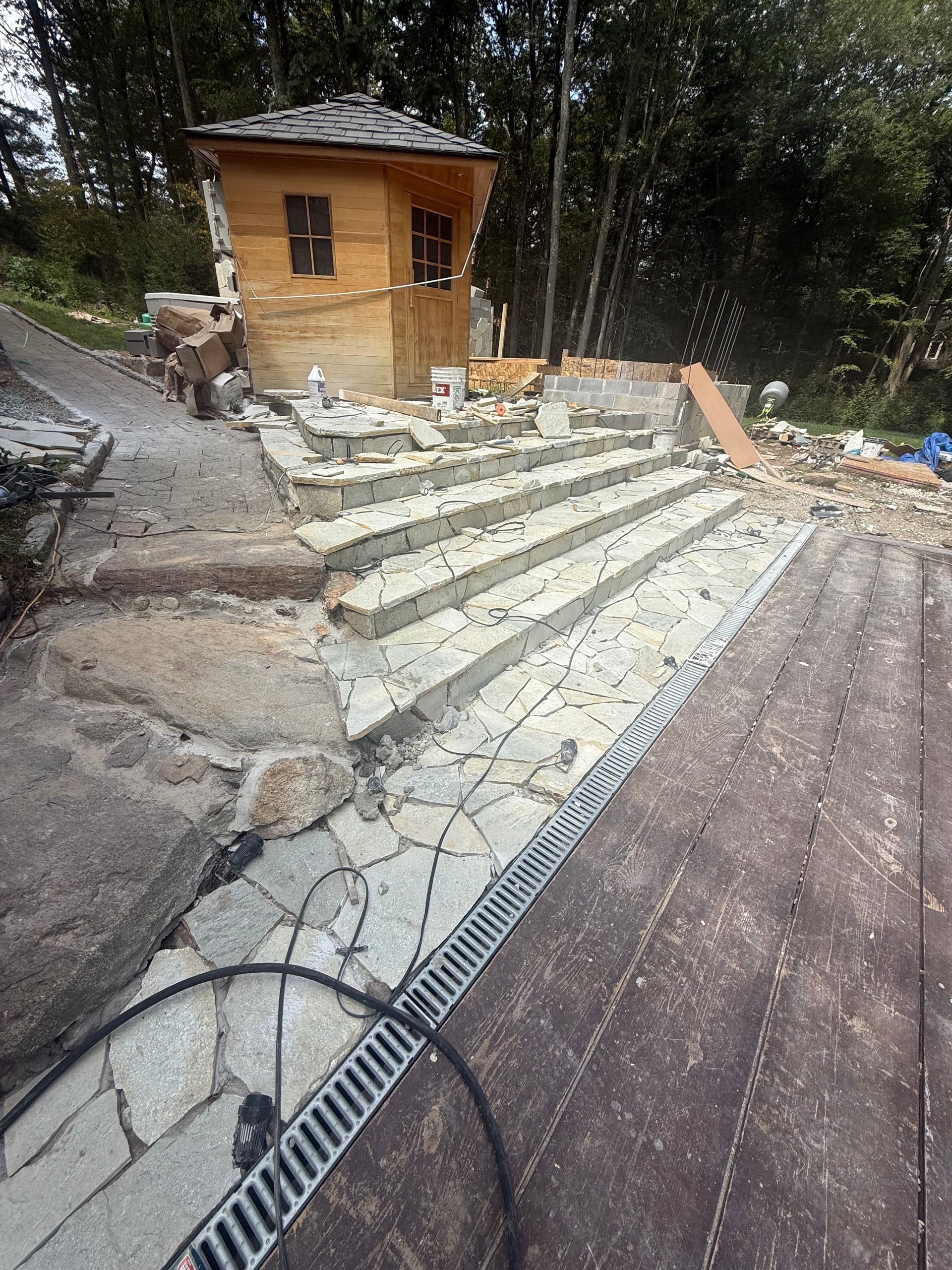 Wooden building and stairs in construction, with a drainage grate in the foreground.