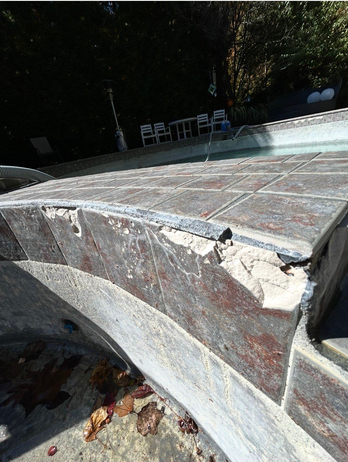 Damaged pool coping with loose tiles and deteriorated mortar, viewed from above.