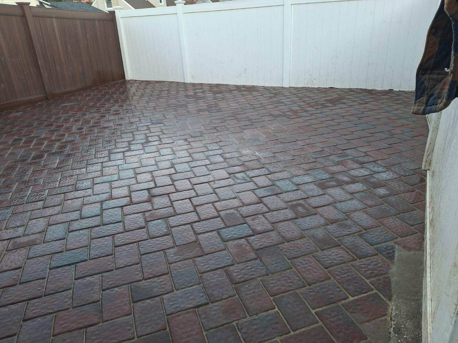 Brick patio with water, enclosed by wooden and white fences.
