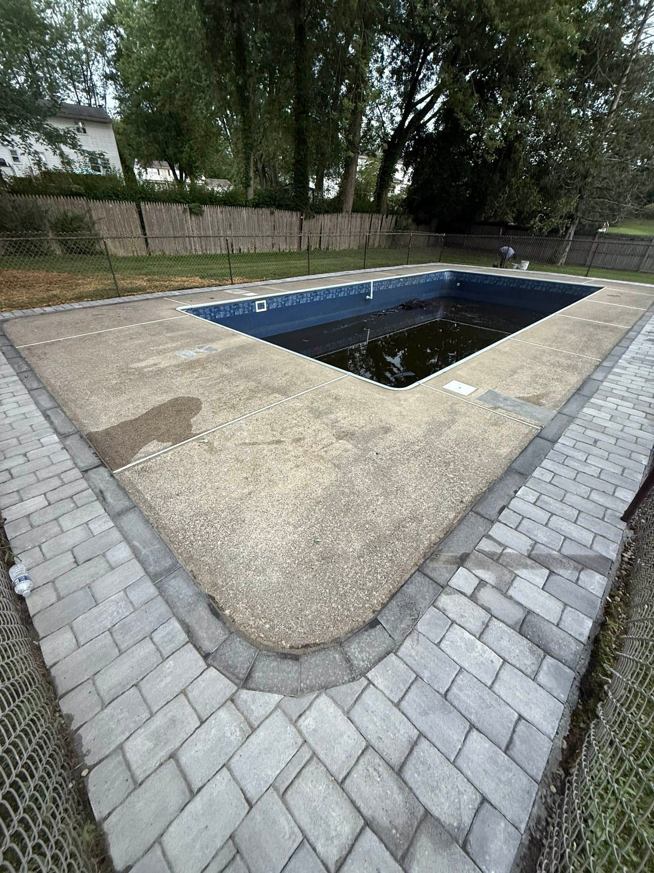 Concrete pool with brick border, surrounded by a chain-link fence and grass.