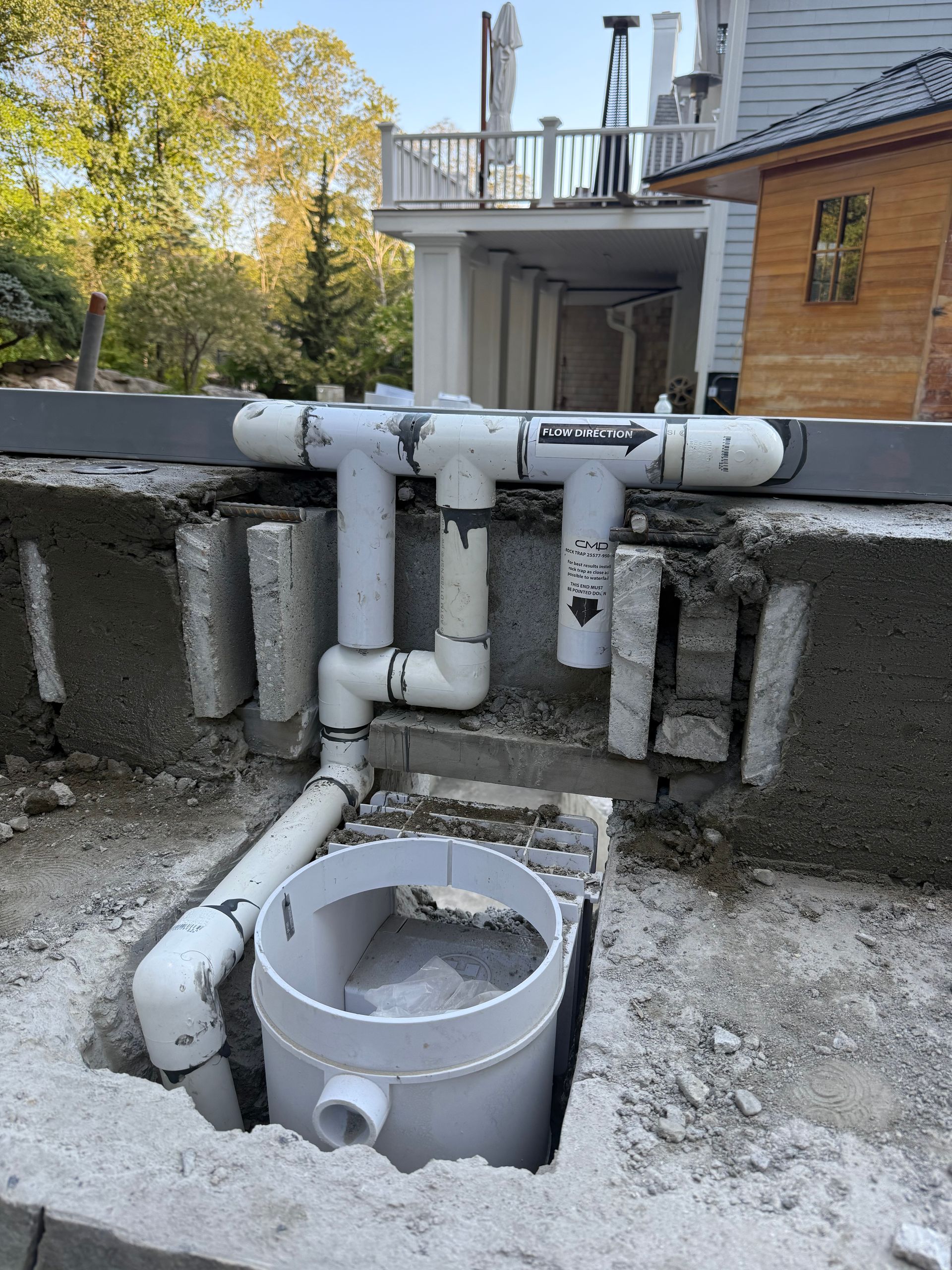 White plumbing pipes and fittings installed in a concrete block structure outdoors, next to a building.