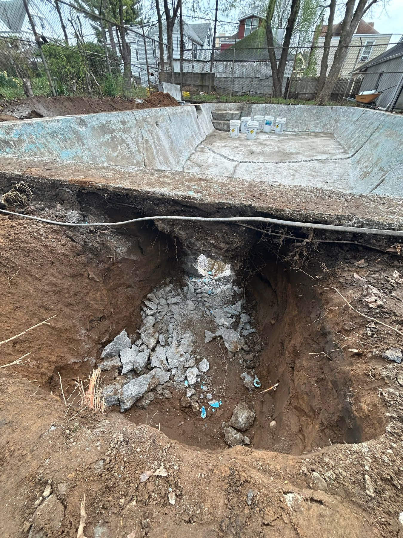 Excavated dirt pit in front of an empty swimming pool. Debris sits in the pit.