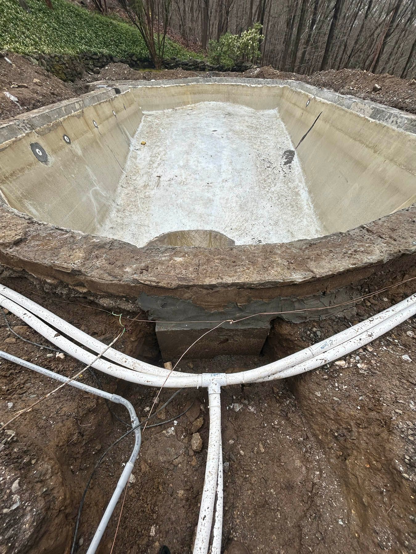 Empty concrete swimming pool under construction, with exposed pipes in foreground.