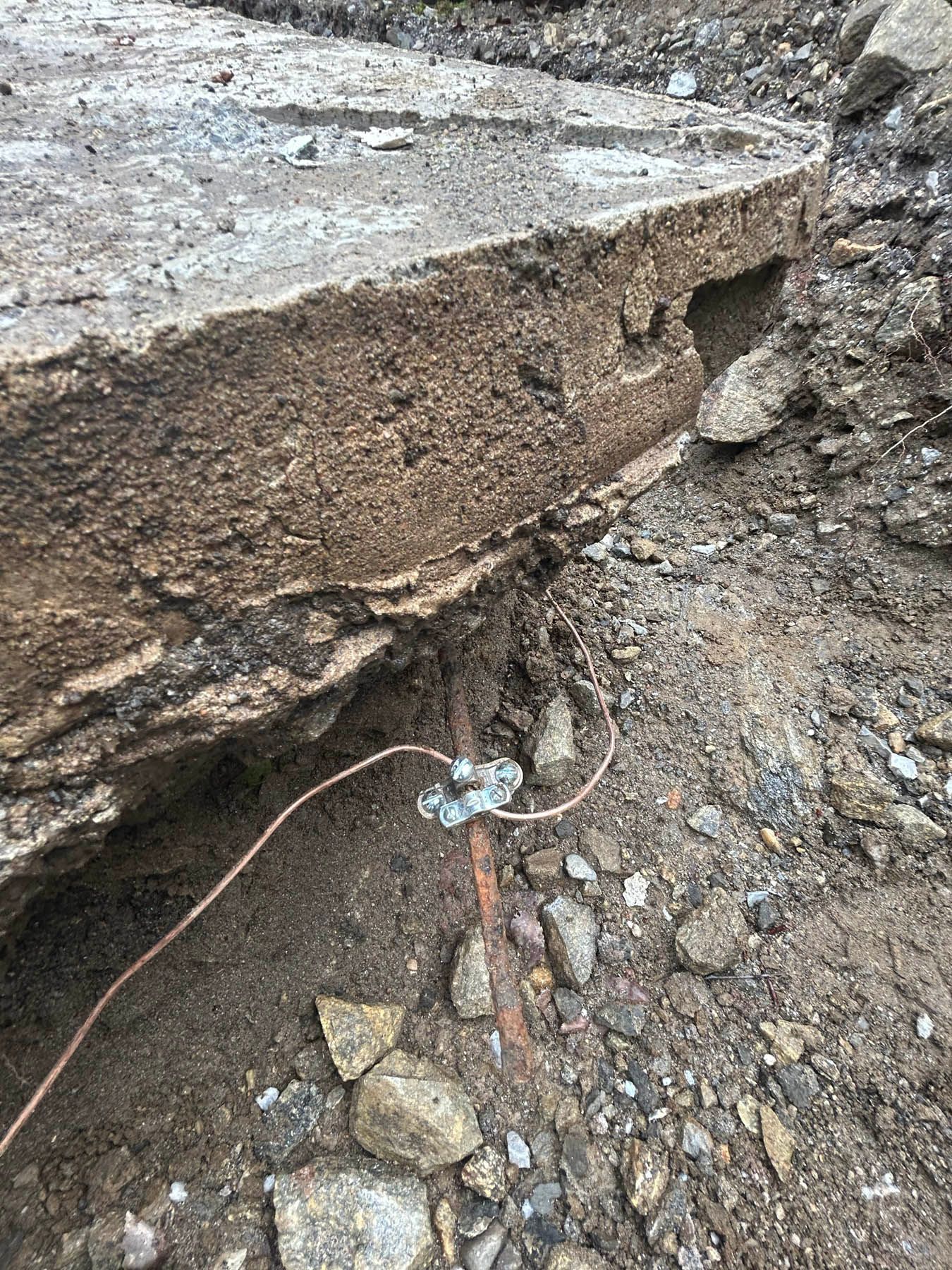 Broken concrete slab with grounding wire attached in a dirt setting.