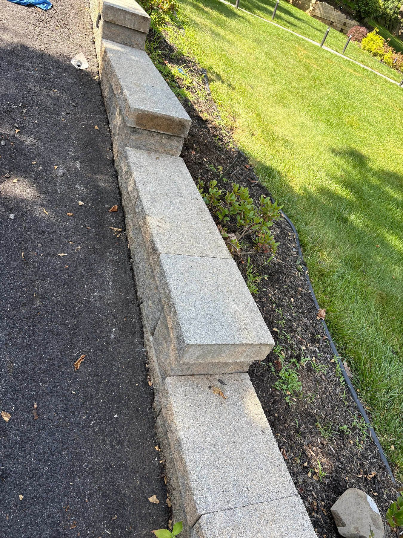 Stone retaining wall next to blacktop and a grassy lawn.