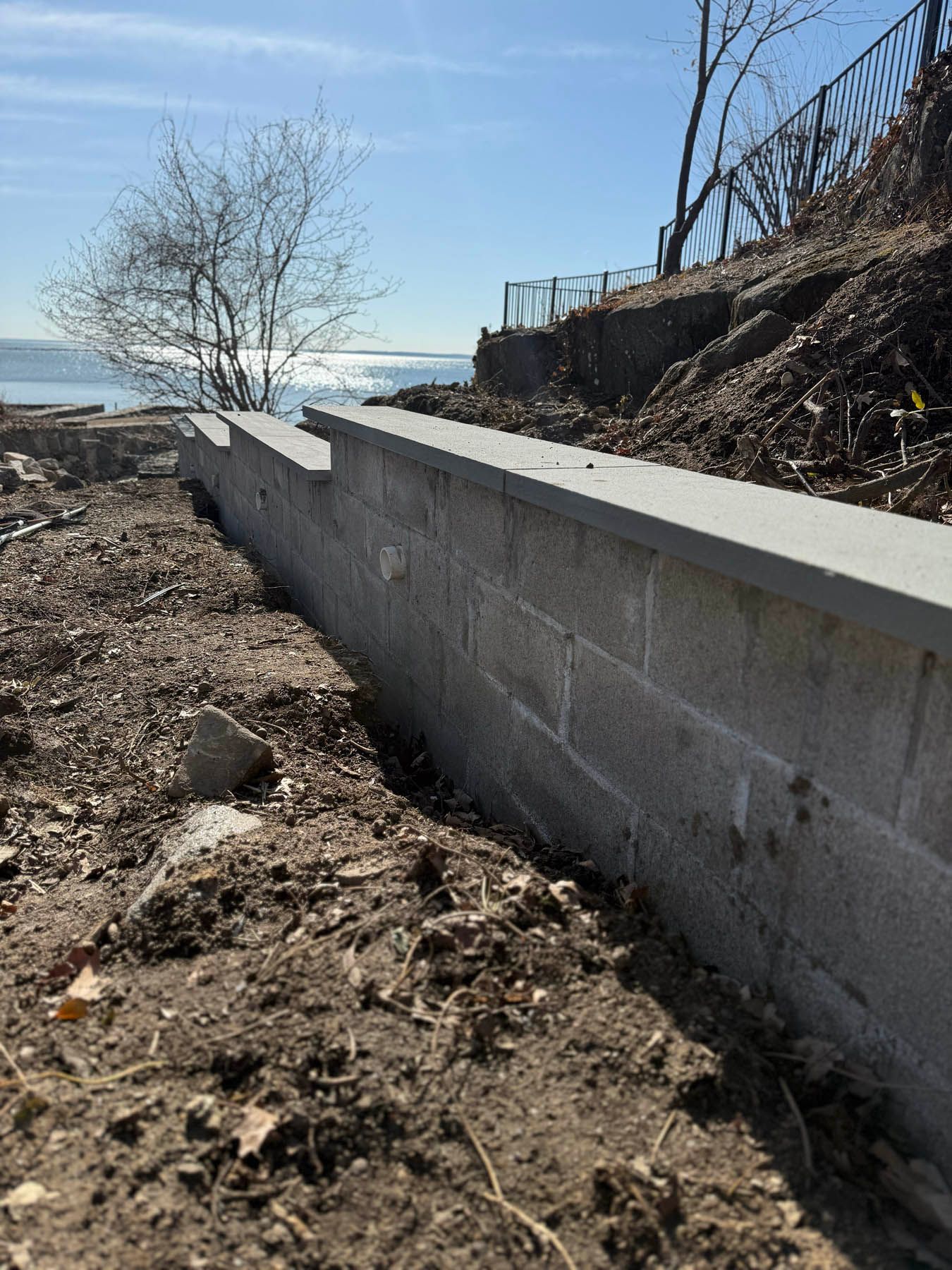 Concrete retaining wall along a shoreline with blue sky and water.