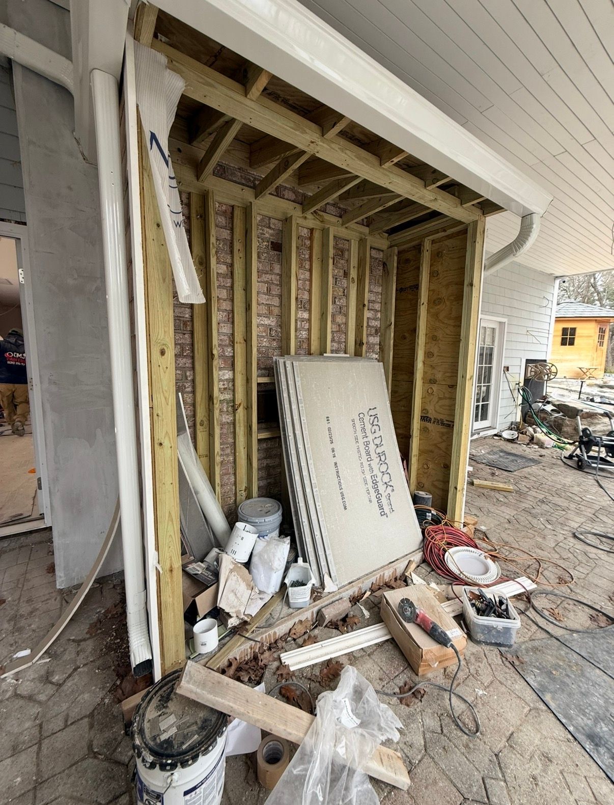 Construction site with exposed framing, materials, and debris. Exterior porch renovation in progress.