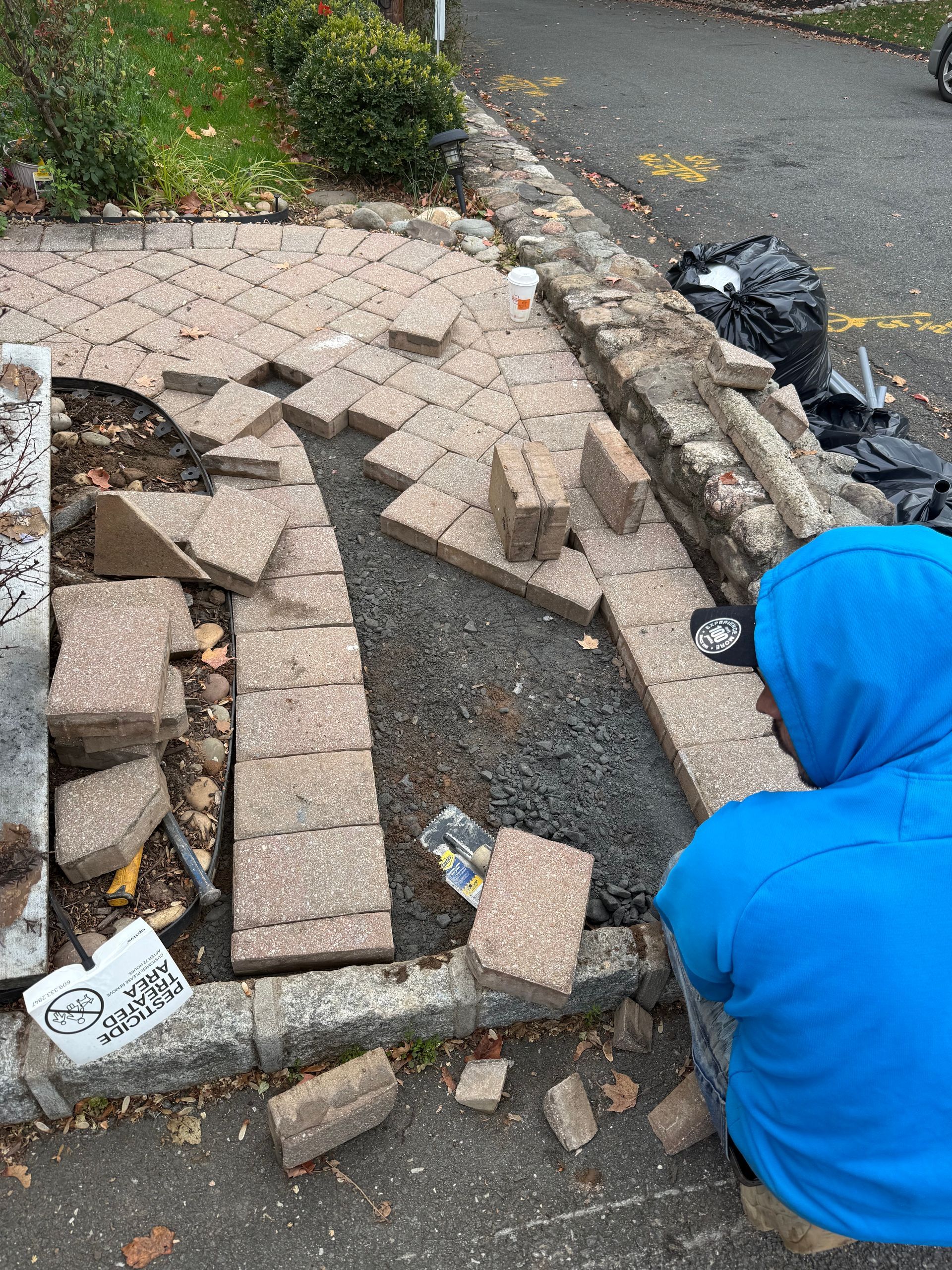 Person in blue hoodie rebuilding a brick walkway next to a stone wall. Debris is scattered.