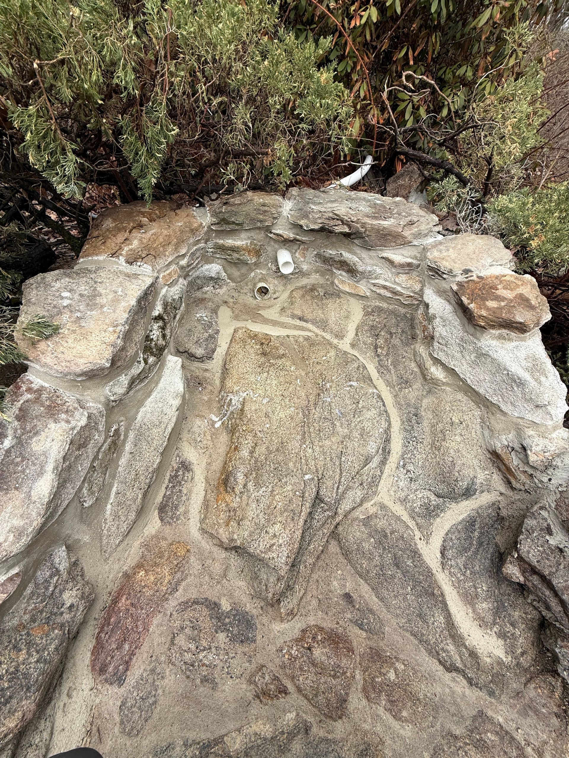 Stone structure with cement mortar, beneath green shrubbery.