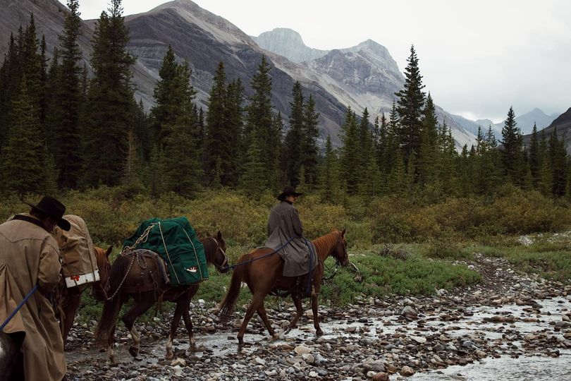 A man riding a horse in a field with mountains in the background