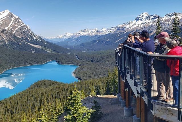 A group of people are standing on a balcony overlooking a lake and mountains.