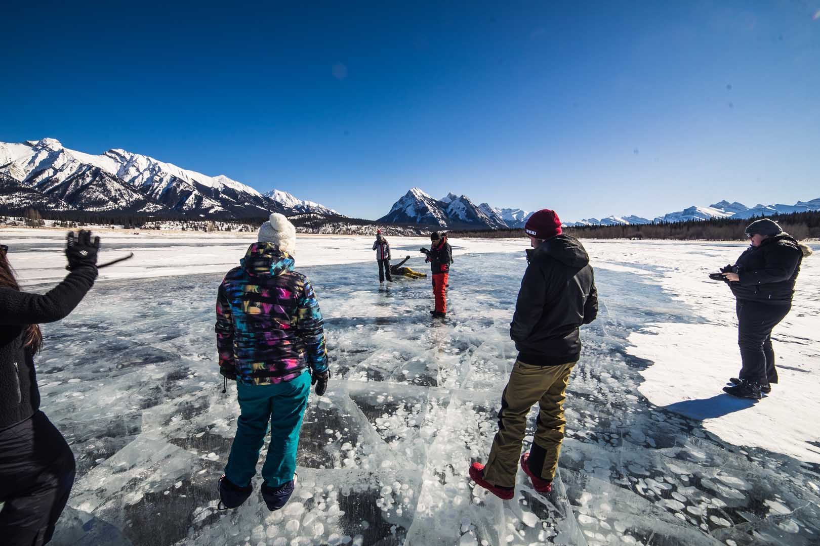 People standing on ice, snowy mountains in the background under a blue sky.