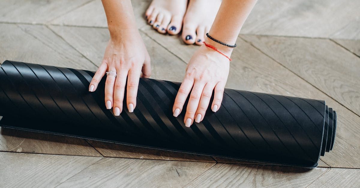 A woman is rolling a black yoga mat on a wooden floor.