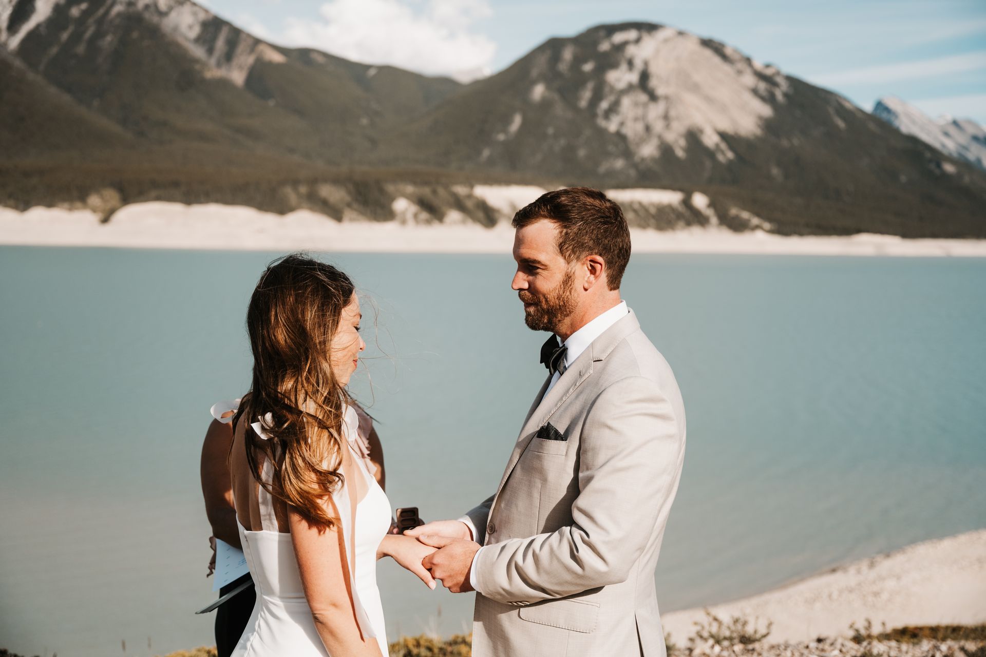 A bride and groom are holding hands during their wedding ceremony in front of a lake.