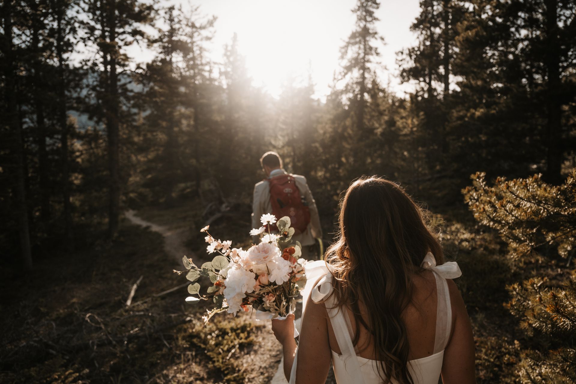 A bride and groom are walking through the woods.