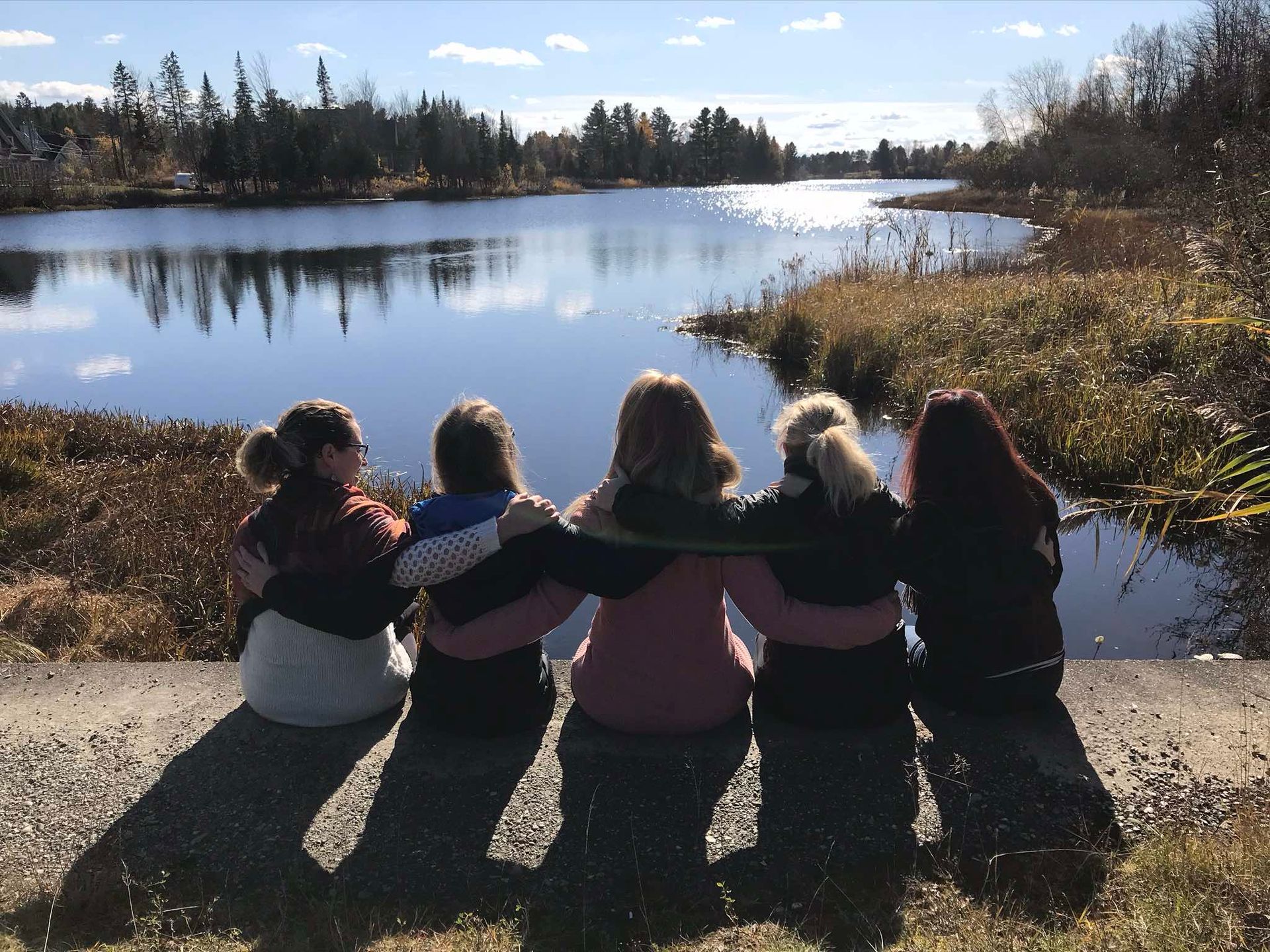 A group of women are hugging and looking at a lake