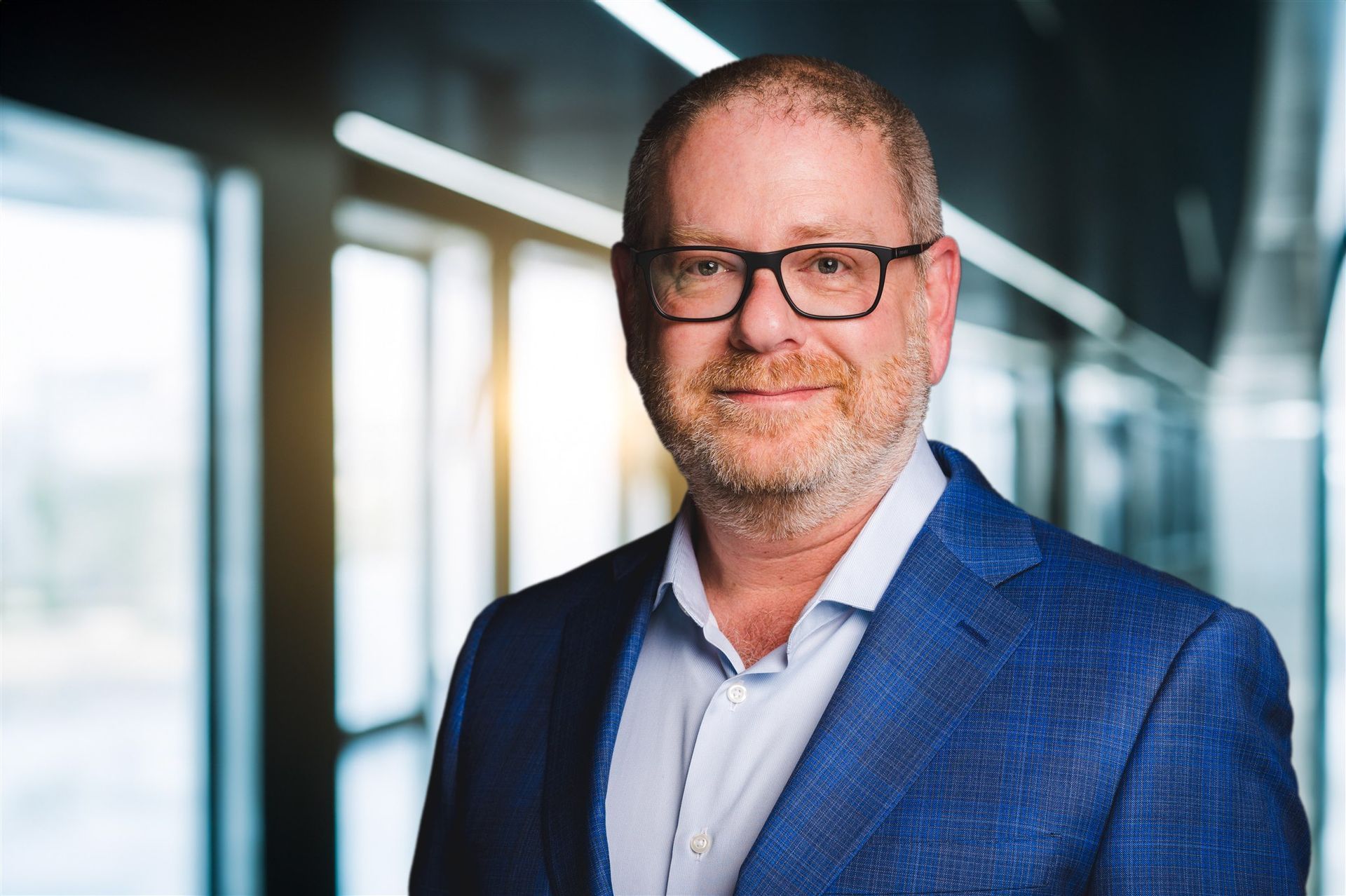 A man in a blue suit and glasses is standing in a hallway.