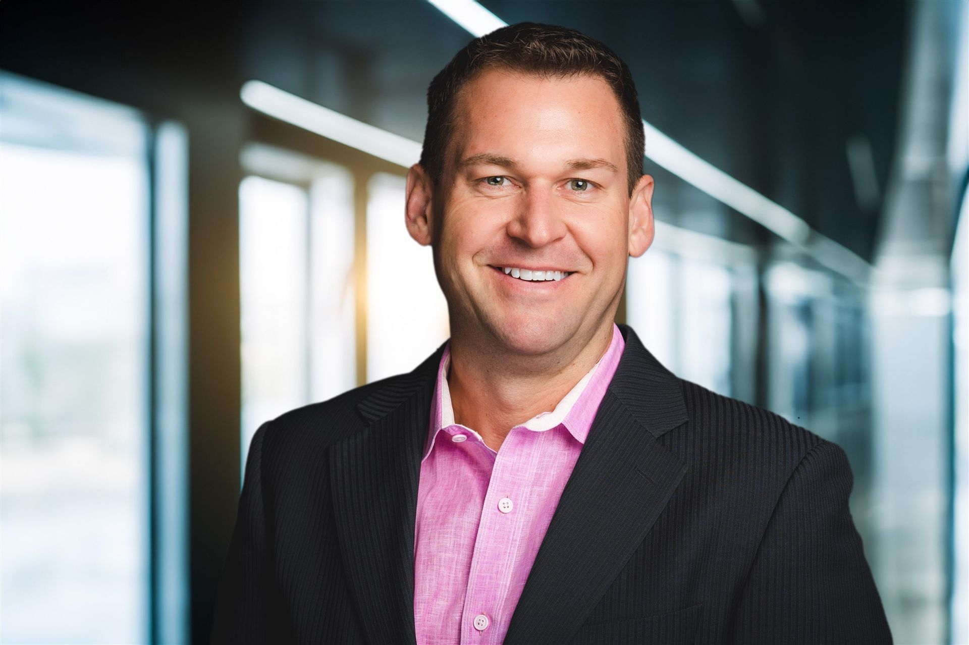 A man in a suit and pink shirt is smiling for the camera.