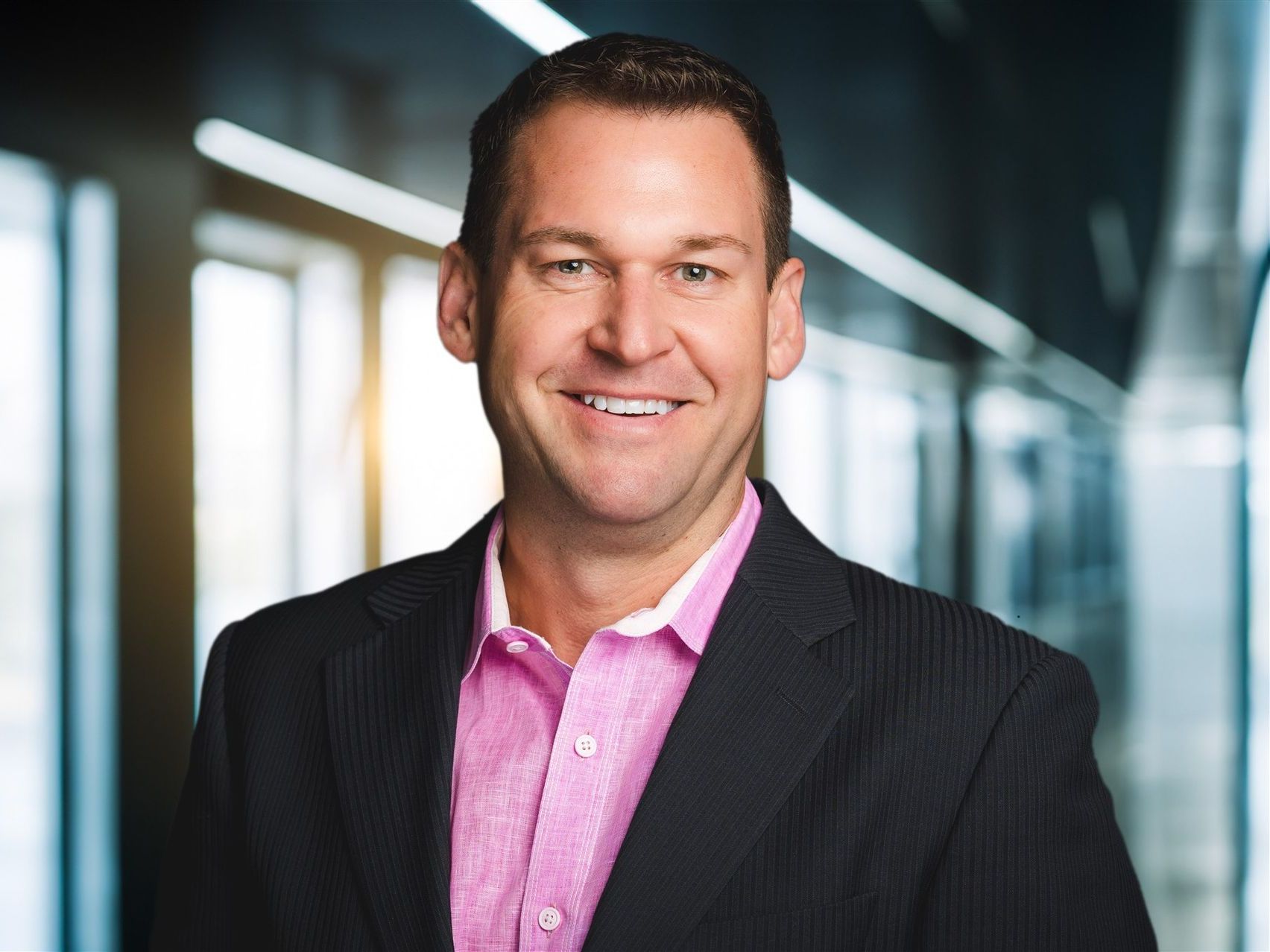 A man in a suit and pink shirt is smiling for the camera.