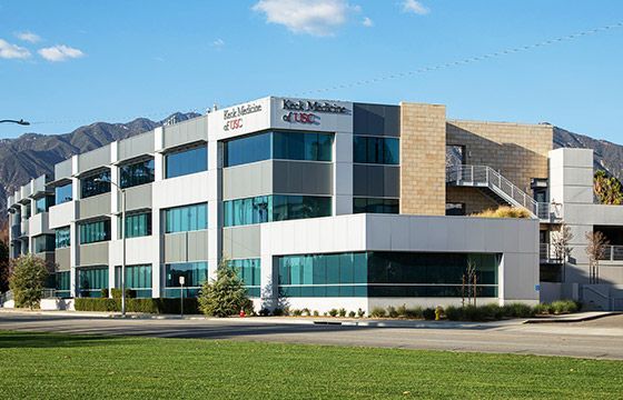 Modern office building with blue-tinted windows, a grassy lawn, and mountains in the background.