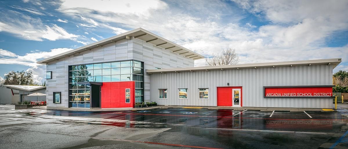 A modern building with a red and gray facade and a glass wall under a blue sky.