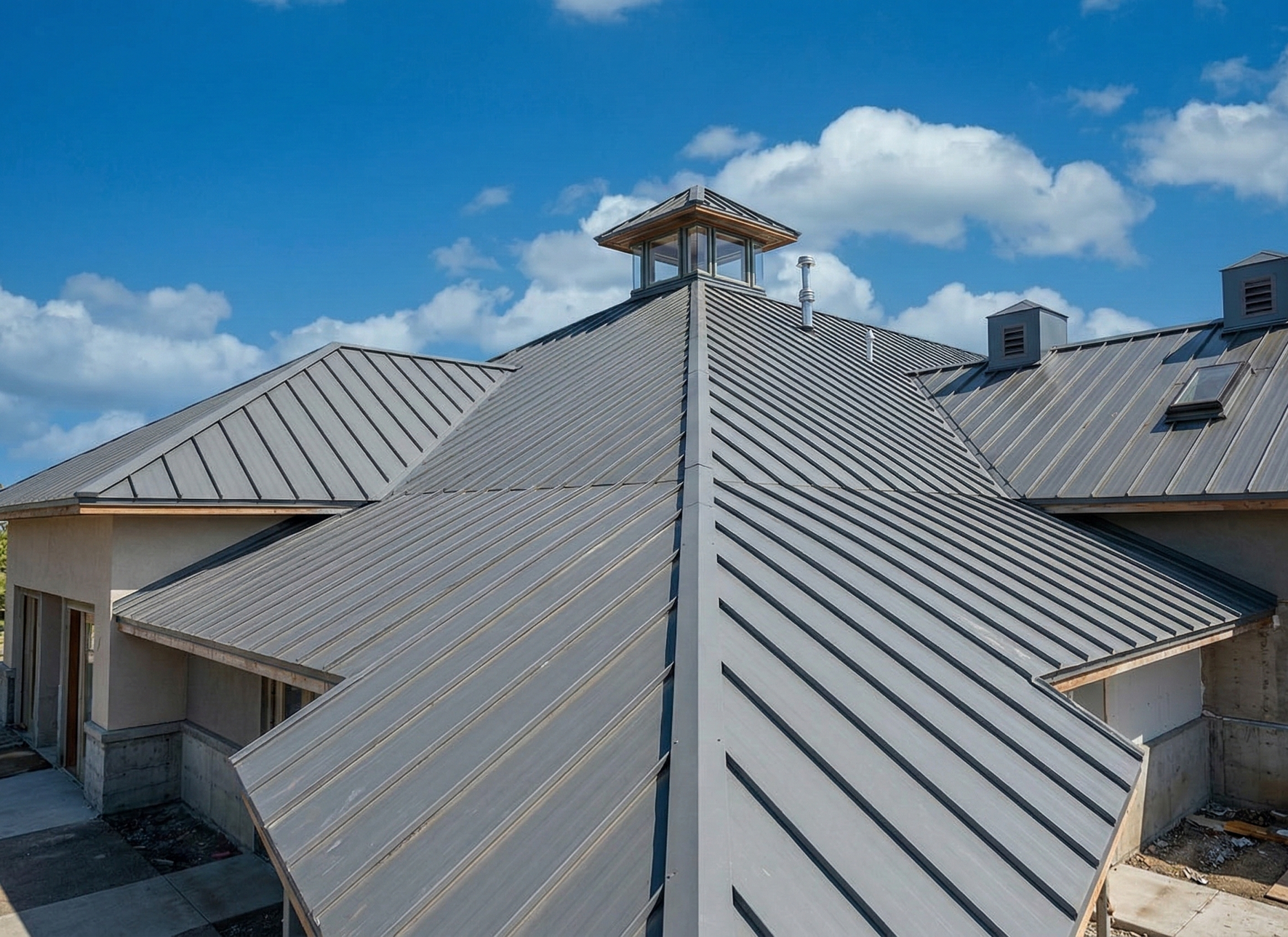Metal roof with skylights and vents against a blue sky with fluffy clouds.