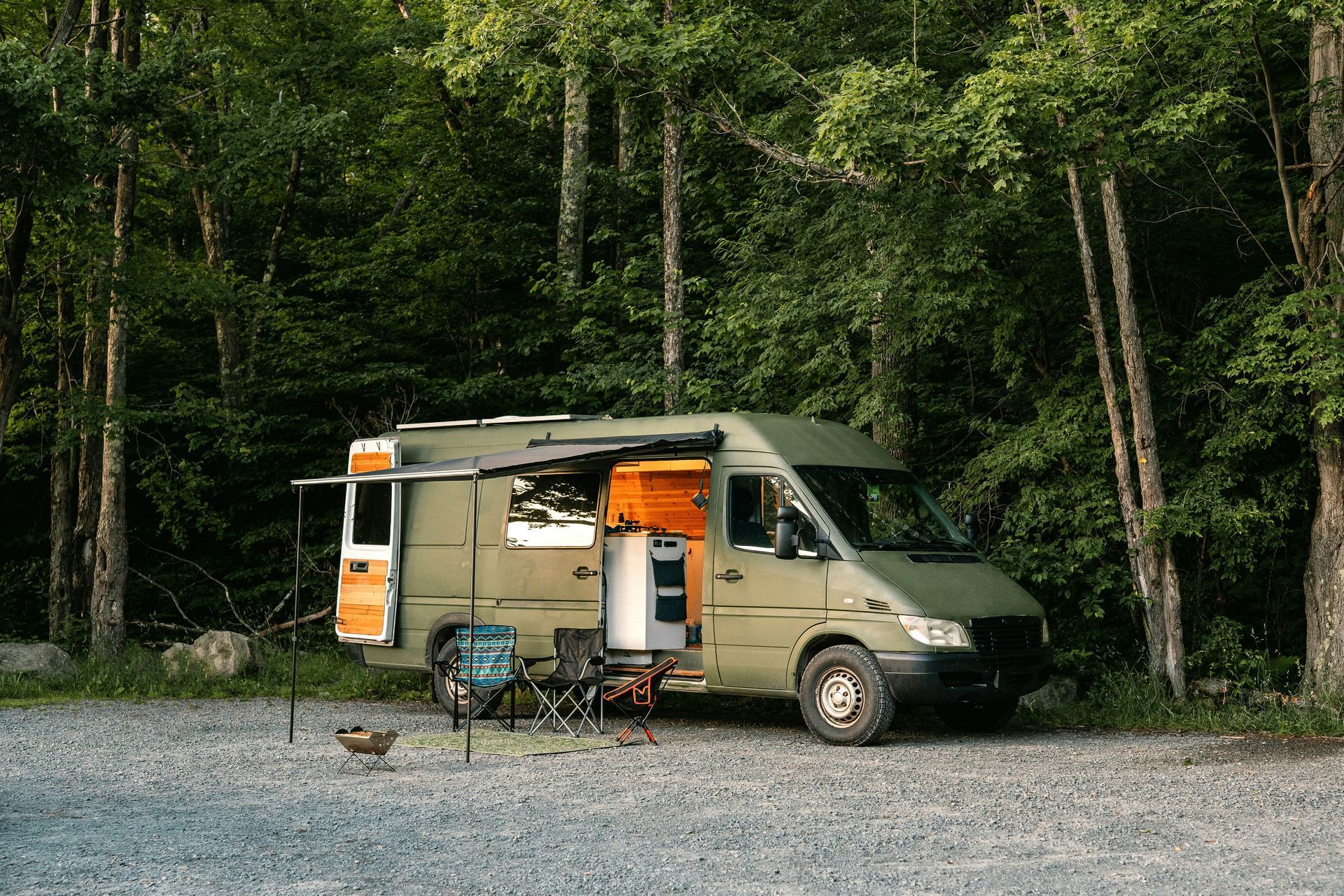 A green van is parked in a gravel lot in the woods.