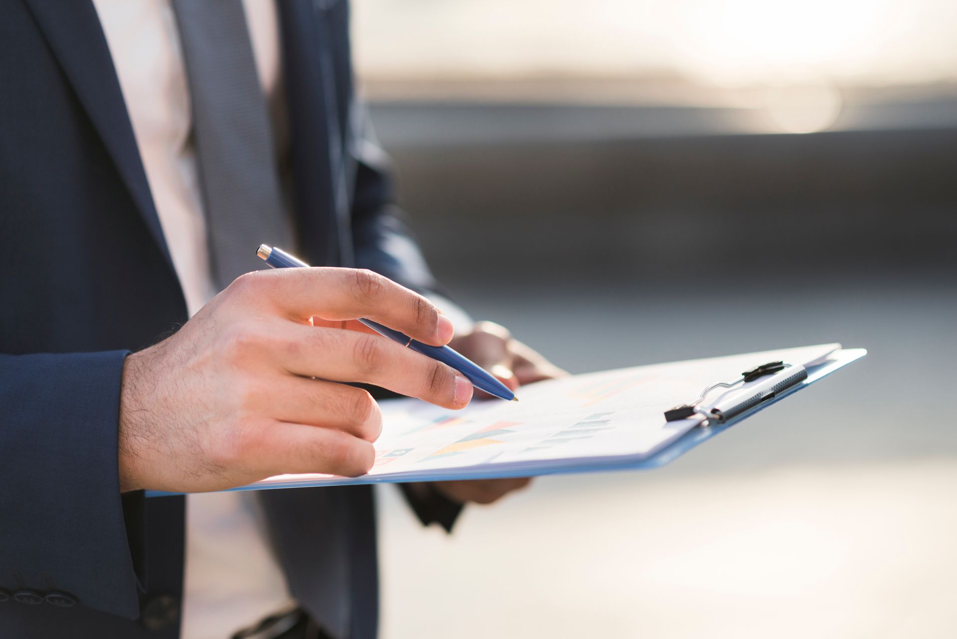 A man in a suit is writing on a clipboard with a pen.